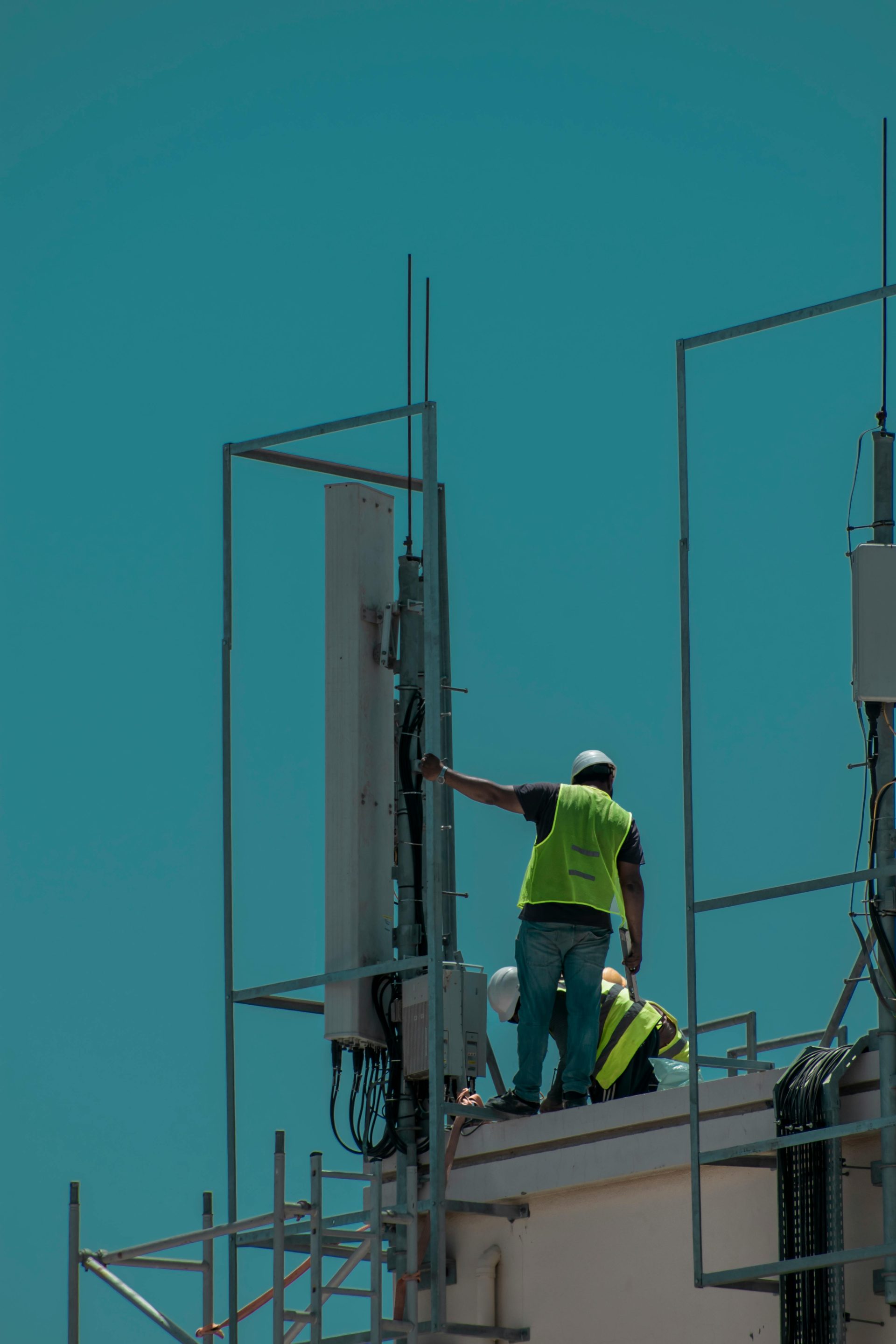 Workers in safety vests on a rooftop in Dubai, installing equipment. Vertical shot.